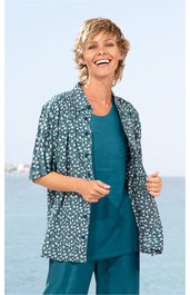 Damenoberteil in Petrol, unifarbenes ärmelloses Langshirt, kombiniert mit locker geschnittener, kurzärmeliger, offener Bluse mit Blumendesign in Dunkelgrün und Weiß, getragen von lächelnder stehender Frau vor hellem Hintergrund