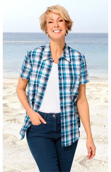 Kurzärmeliges Hemd, karierte Muster in Blau- und Türkistönen, klassischer Hemdkragen, Vorderseite geöffnet, getragen von stehender Frau am Strand, kombiniert mit weißem Unterhemd und dunkler Jeans