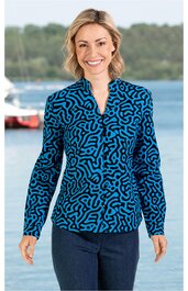 Langarmshirt in leuchtendem Blau mit schwarzem abstraktem Muster, V-Ausschnitt, körpernah geschnitten, getragen von lächelnder stehender Frau vor Wasser, gerade geschnittener Saum