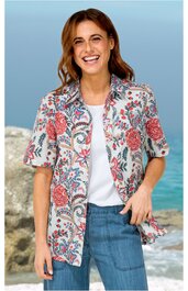 Kurzärmeliges Hemd in Weiß mit buntem Blumenmuster in Rot, Blau und Grün, Kragen, durchgehende Knopfleiste, getragen von lächelnder stehender Frau, offene Vorderseite, kombiniert mit weißem T-Shirt und blauer Hose