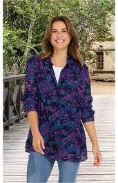 Blau-violettes langärmeliges Hemd mit lila und pinkem Blumenmuster, Kragen, knöpft vorne, locker geschnitten, getragen von stehender Frau, dazu weiße Innenbluse und blaue Jeans