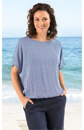 Hellblaues, locker geschnittenes Shirt mit feinem Streifenmuster, rundem Ausschnitt, kurze Ärmel mit offener Seitennaht, getragen von stehender Frau am Strand, elastischer Saum