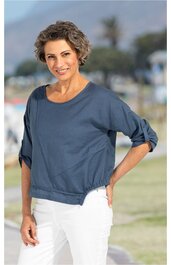 Marineblaues Sweatshirt mit rundem Ausschnitt, langen Ärmeln mit aufgekrempelten Bündchen, tailliert geschnitten, getragen von stehender Frau mit kurz gelocktem Haar, weiße Hose