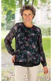 Langärmlige Bluse schwarz mit buntem Blumenmuster, rundem Halsausschnitt, locker geschnitten, getragen von lächelnder stehender Frau mit kurzen lockigen Haaren