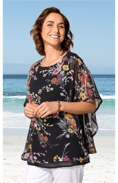 Schwarze Tunika mit buntem Blumenmuster, rundem Ausschnitt, kurzen weiten Ärmeln, locker sitzend, getragen von lächelnder stehender Frau am Strand