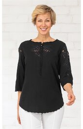 Schwarze Bluse mit Rundhalsausschnitt und kurzer Knopfleiste, 3/4-Ärmel mit Lochmuster, lockere Passform, gewellter Saum, getragen von stehender Frau