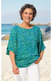Türkisgrüne Bluse mit abstraktem Muster, rundem Ausschnitt, weite kurze Ärmel, locker geschnitten, getragen von lächelnder Frau am Strand, weiße Hose