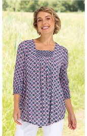 Langarmshirt in Weiß und Dunkelblau mit rosa Akzenten, geometrisches Muster aus Rauten, quadratischer Ausschnitt, leichte Falten am Brustbereich, gerade geschnitten, getragen von lächelnder Frau stehend