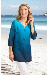 Blaues Langarmshirt mit floralem Muster, Rundhalsausschnitt mit kleinem Schlitz, locker geschnitten, getragen von stehender Frau am Strand