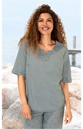 Hellgraue Bluse mit kurzen Ärmeln, V-Ausschnitt mit Zierstickerei, gerade geschnitten, getragen von lächelnder Frau vor Meereskulisse