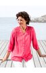 Rosa Bluse mit Spitzenbesatz an Schultern und Saum, durchgehende Knopfleiste, V-Ausschnitt, 3/4-ärmel, lockere Passform, getragen von sitzender Frau vor Meereskulisse