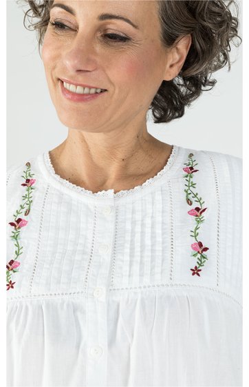 Weißes Damenoberteil mit feiner vertikaler Struktur, Blumenstickerei entlang des Rundhalsausschnitts, leichter Stehkragen mit Spitzenkante, getragen von Frau im Porträt, locker sitzend