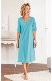 Türkisblaues Nachthemd ohne Muster, V-Ausschnitt, halblange Ärmel, knielang, locker sitzend, getragen von stehender Frau mit hochgekrempelten Haaren, barfuß