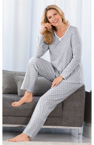 Grauer Pyjama mit weißem Punktemuster, langer Arm, V-Ausschnitt mit Knopfdetail, lange Hose, getragen von sitzender Frau auf grauem Sofa