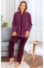 Hausanzug dunkelrot einfarbig, langärmlige Jacke mit Stehkragen und Reißverschluss, zwei aufgesetzte Taschen, gerade geschnittene Hose, getragen von sitzender lächelnder Frau