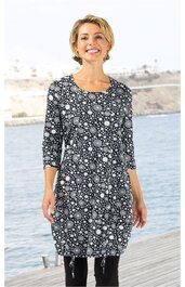 Schwarzes Kleid mit weißem Kreis- und Punktemuster, Rundhalsausschnitt, 3/4-lange Ärmel, knieumspielend, gerade geschnitten, getragen von lächelnder Frau, stehende Pose am Wasserufer