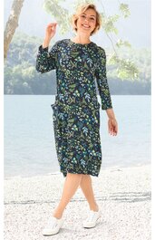 Knieumspielendes Kleid in dunkelblau mit buntem Blumenmuster, rundem Halsausschnitt, 3/4-Ärmel, gerade geschnitten, getragen von stehender lächelnder Frau mit weißen Sneakers