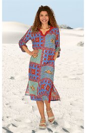 Midikleid mit V-Ausschnitt, dreiviertel Ärmeln, geblümtem und geometrischem Patchworkmuster in Rot, Blau, Hellblau und Beige, seitlichem Schlitz, getragen von stehender Frau mit Locken, Sandstrand im Hintergrund