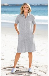 Kleid in Hellgrau mit weißen senkrechten Streifen, Hemdblusenkragen, halblange Ärmel, durchgehende Knopfleiste vorne, knieumspielend, getragen von lächelnder stehender Frau am Strand, seitliche Eingrifftaschen