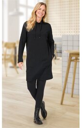 Schwarzes Kapuzenkleid ohne Muster, lange Ärmel, seitliche Taschen, locker geschnitten, getragen von stehender Frau, kombiniert mit schwarzen Leggings und schwarzen Schnürstiefeln