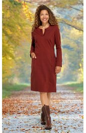 Dunkelrotes knielanges Kleid mit V-Ausschnitt, lange Ärmel, aufgesetzten Taschen vorne, gerade geschnitten, getragen von stehender Frau in herbstlicher Waldlandschaft, kombiniert mit braunen Stiefeletten
