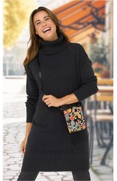 Schwarzes Rollkragen-Strickkleid mit langen Ärmeln, Rippstrick an Ärmeln und Saum, knielang, getragen von lächelnder stehender Frau, schwarze Umhängetasche mit farbigem Blumenmuster und Reißverschluss
