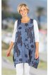 Ärmellose Tunika in dunklem Blau mit großem blauen Blumenmuster, Rundhalsausschnitt, asymmetrischer Saum, getragen von stehender lächelnder Frau mit weißen 3/4-Ärmeln und weißer Hose
