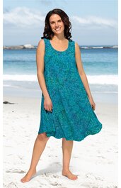 Locker sitzendes, ärmelloses Sommerkleid in petrolblau mit floralem Muster, Rundhalsausschnitt, knielang, getragen von stehender Frau am Strand, fließender Saum