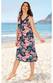 Ärmelloses Midikleid in dunkelblau mit großflächigem pink-weiß-grünem Blumenmuster, V-Ausschnitt, taillierter Schnitt, leichte A-Linien-Form, getragen von stehender Frau am Strand, knielang