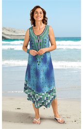 Ärmelloses sommerliches Midikleid in Blau- und Grüntönen mit abstraktem Muster, V-Ausschnitt, asymmetrischer Saum, getragen von stehender Frau am Strand, lässig geschnitten