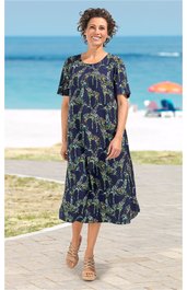 Dunkelblaues Midikleid mit grünem Blumenmuster, Rundhalsausschnitt, kurze Ärmel, locker geschnitten, getragen von stehender Frau am Strand, Saum mit leichter Rüsche
