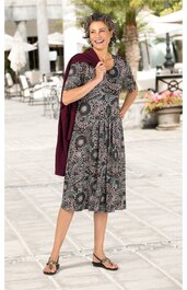 Knieumspieltes Kleid mit kurzen Ärmeln, dunkelgrau mit rundem floralen Muster in Hellrosa und Weiß, Rundhalsausschnitt, leichter Faltenwurf am Rock, getragen von stehender Frau, bordeauxroter Schal über eine Schulter gelegt, offene Sandalen