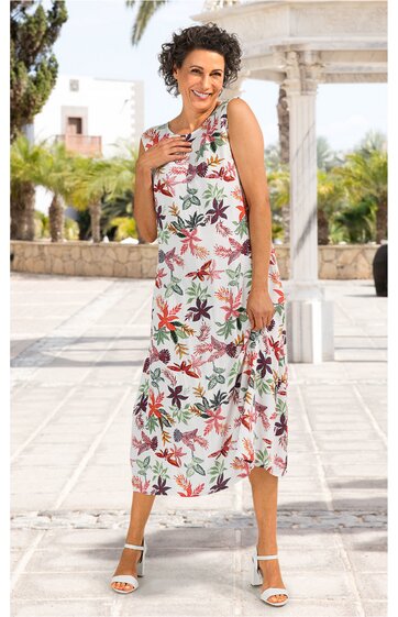 Ärmelloses, knöchellanges Sommerkleid in Weiß mit buntem Blumenmuster, rundem Ausschnitt, lockere Passform, getragen von stehender Frau, seitlicher Schlitz, sommerliche Sandalen weiß