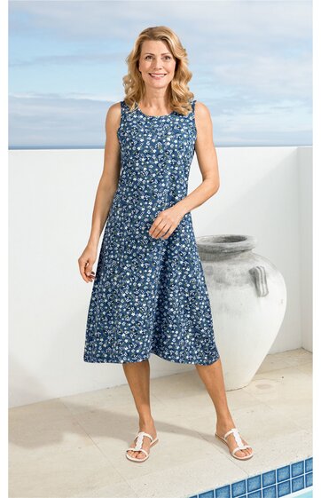 Blaues ärmelloses Kleid mit weißem Blütenmuster, Rundhalsausschnitt, knielang, ausgestellter Rock, getragen von stehender Frau in Sandalen