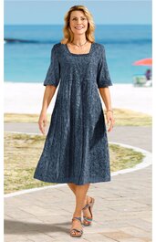 Dunkelblaues Midikleid mit floralem Muster, rundem Ausschnitt, halbhohen Ärmeln, ausgestellter Schnitt, getragen von lächelnder stehender Frau im Sandalen am Strand