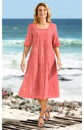 Korallenrotes Maxikleid mit strukturiertem Muster, U-Ausschnitt, halblange Ärmel, locker sitzende A-Linien-Form, getragen von stehender Frau am Strand, knöchelhoch