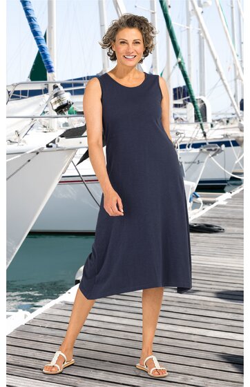 Ärmelloses, dunkelblaues Midikleid mit rundem Ausschnitt, locker fallend, figurumspielend, getragen von einer lächelnden Frau stehend auf Holzsteg vor weißen Segelbooten, weiße Sandaletten