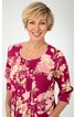Magentafarbenes Damenoberteil mit beigem Blumenmuster, U-Ausschnitt, 3/4-Ärmel, lockere Passform, vorne Teilungsnähte, getragen von lächelnder stehender Frau