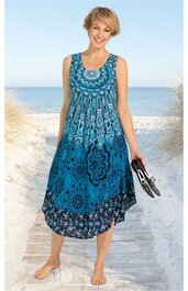Ärmelloses midilanges Kleid in Blau mit dunkelblauem und hellblauem Blumen- und Ornamentmuster, runder Ausschnitt, locker fallend, getragen von stehender Frau am Strand, asymmetrischer Saum