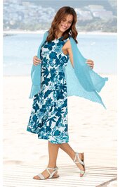 Ärmelloses, knielanges Kleid mit Blumenmuster in Weiß und Blau, Rundhalsausschnitt, ausgestellter Rock, getragen von lächelnder stehender Frau am Strand, offene Strickjacke in Hellblau, weiße Sandalen
