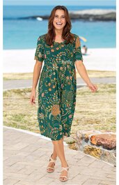 Kleid in Grün mit floralem Muster in Hellbraun, kurze Ärmel, Rundhalsausschnitt, knielang, ausgestellte Form, getragen von stehender Frau am Strand
