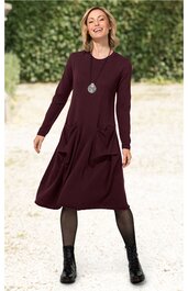 Bordeauxrotes Kleid, einfarbig, lange Ärmel, Rundhalsausschnitt, ausgestellter Rock, zwei Taschen vorne, getragen von lächelnder Frau in aufrechter, lockerer Pose, kombiniert mit schwarzen Strumpfhosen und schwarzen Schnürstiefeln