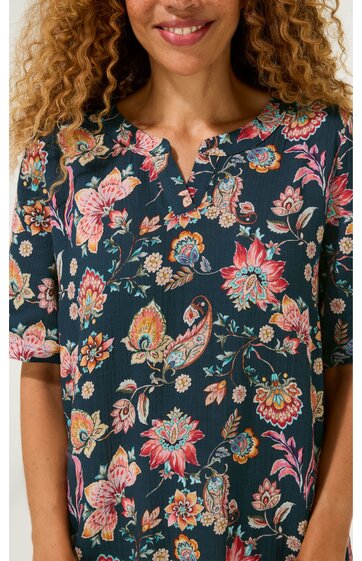 Dunkelgrünes Kleid mit buntem Blumenmuster, kurze Ärmel, Rundhals mit kleinem V-Ausschnitt, locker sitzend, getragen von Oberkörper einer lächelnden Frau