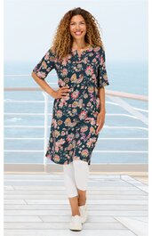 Dunkelblaues Midikleid mit floralem Muster in Rosa und Beige, Rundhals, halblange Ärmel, gerade geschnitten, getragen von stehender Frau mit lockerem Haar, kombiniert mit weißen Leggings und weißen Sneakers