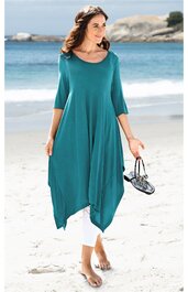 Türkisfarbenes, asymmetrisches Kleid mit 3/4-Ärmeln, rundem Ausschnitt, locker sitzend, getragen von stehender Frau am Strand, detailreich fallende Saumkanten