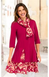 Fuchsiafarbene Tunika mit dreiviertel Ärmeln, floral gemustertes Unterkleid in Rot und Creme, asymmetrischer Schnitt mit Raffung, getragen von stehender lächelnder Frau