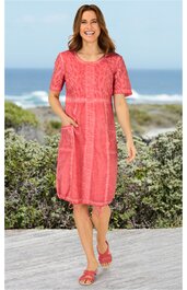 Rotes knielanges Kleid mit floralem Muster, halblange Ärmel, Rundhalsausschnitt, seitliche Eingrifftaschen, locker sitzend, getragen von lächelnder stehender Frau