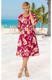 Rotes knielanges Kleid mit beigem großen Blumenmuster, Rundhals, dreiviertellange Ärmel, Taschen, weit geschnitten, getragen von stehender Frau am Strand