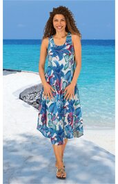 Ärmelloses, knielanges Sommerkleid in Blau und Weiß mit floralem Muster, rundem Ausschnitt, lockerer Schnitt, getragen von stehender Frau am Strand mit Sand und Meer im Hintergrund