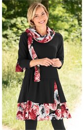 Schwarzes Kleid mit dreiviertel Ärmeln, ausgestelltem Rockteil, mit roten, weißen und grauen Blumenmustern am Rocksaum und passendem Blumenschal, getragen von lächelnder Frau im Stehen, tailliert